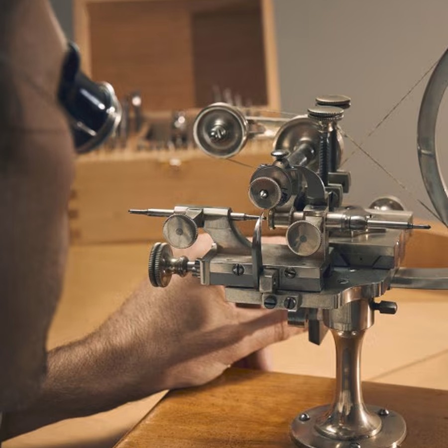 Craftsman inspecting a mechanical part through a loupe while working  on a traditional watchmaking lathe.