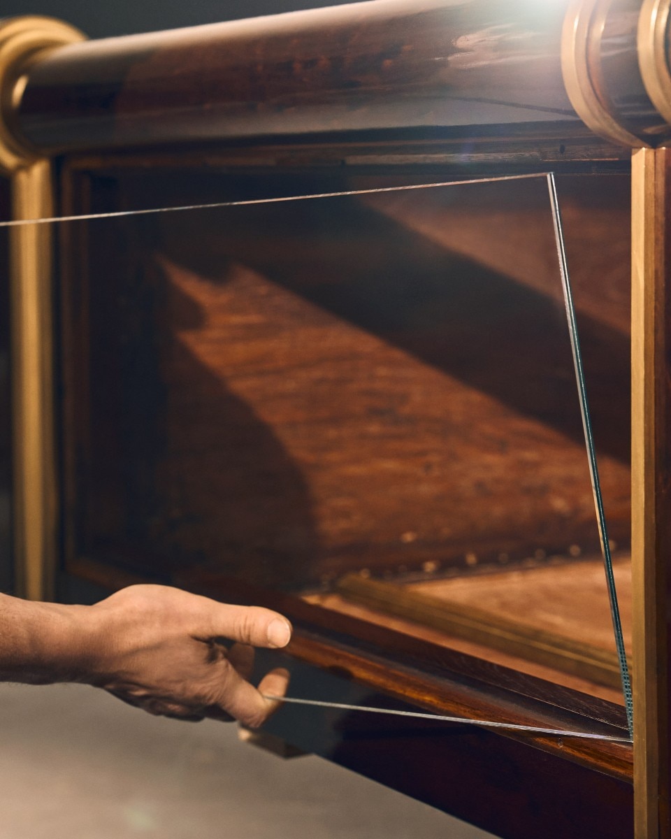 Restorer adjusting a drawer front on an ornate wooden cabinet with golden details.