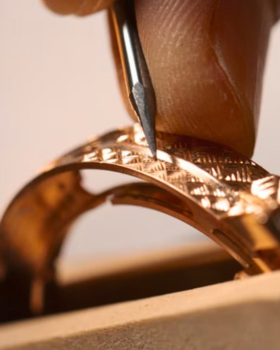 自然资源 Detailed view of a hand engraving a decorative pattern onto a golden watch case using a specialized tool.