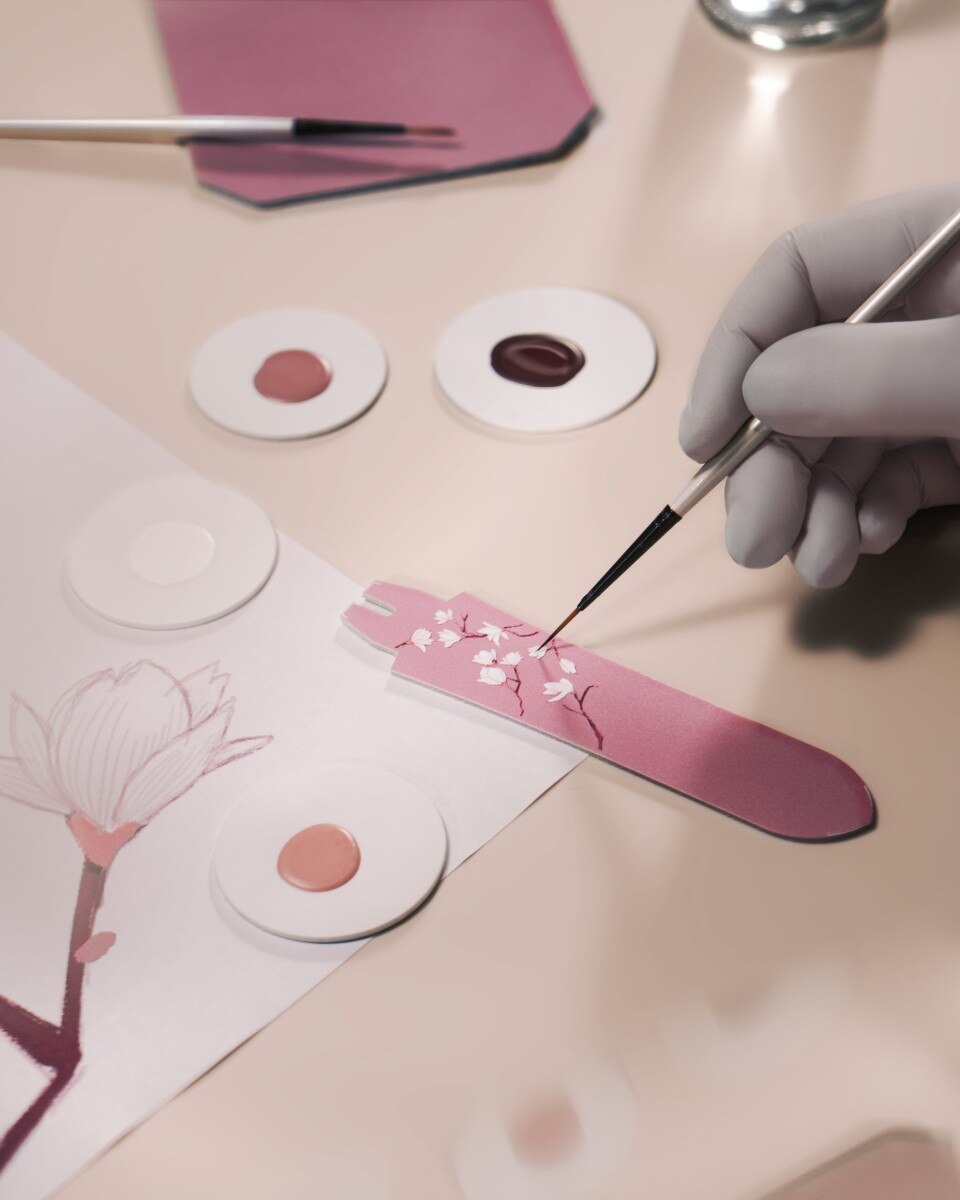 Artisan hand-painting pink floral elements on the dial of the Egerie Moon Phase Spring Blossom watch.