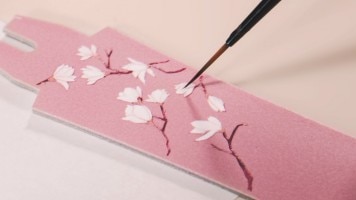 An artist paints floral motifs on a Egerie Moon Phase Spring Blossom watch strap with a brush.
