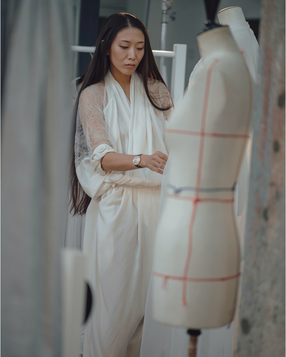 Woman in a light silk outfit fitting a mannequin, wearing a Vacheron Constantin watch on her wrist.