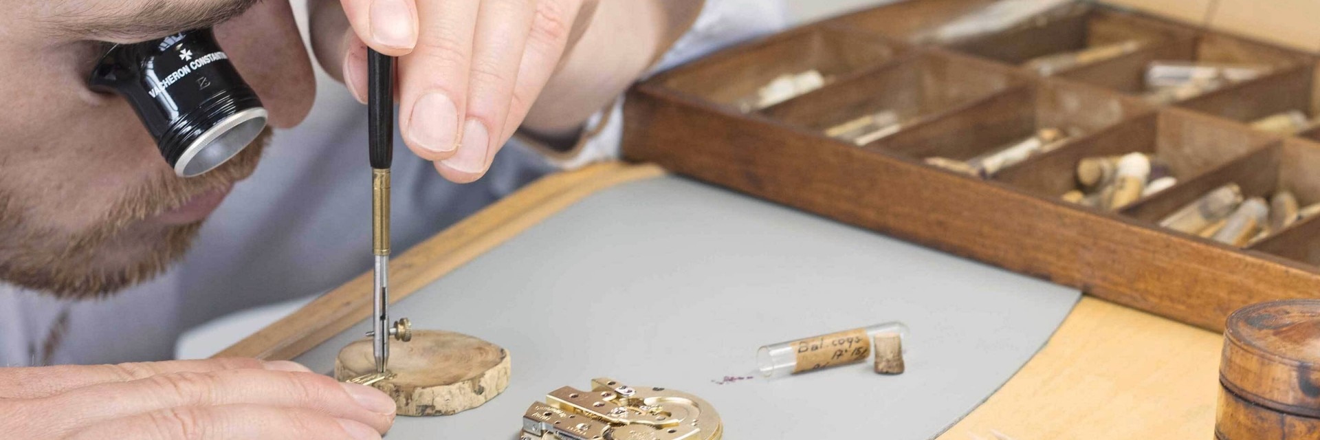 制表师使用螺丝刀在木制工作台上使用井然有序的工具组装钟表零件。