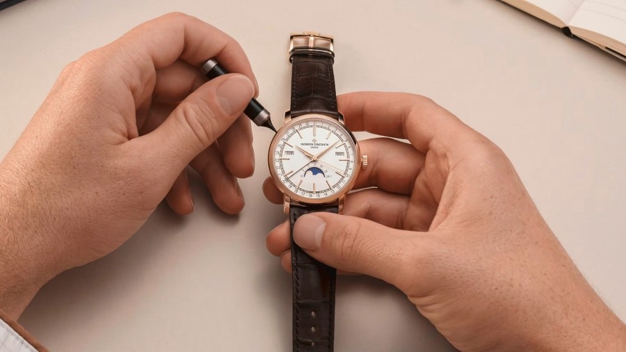 Two hands in white gloves are setting up a watch with a green dial with gold details