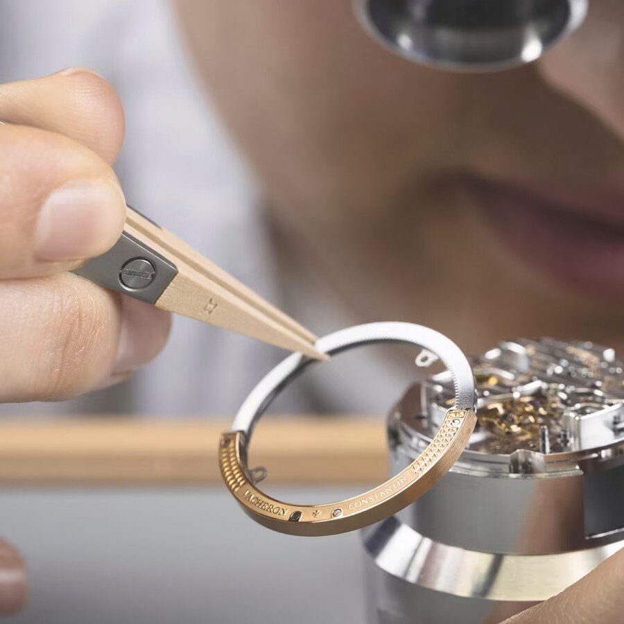 Watchmaker assembling a watch component under a microscope, using precision tweezers and wooden tools.