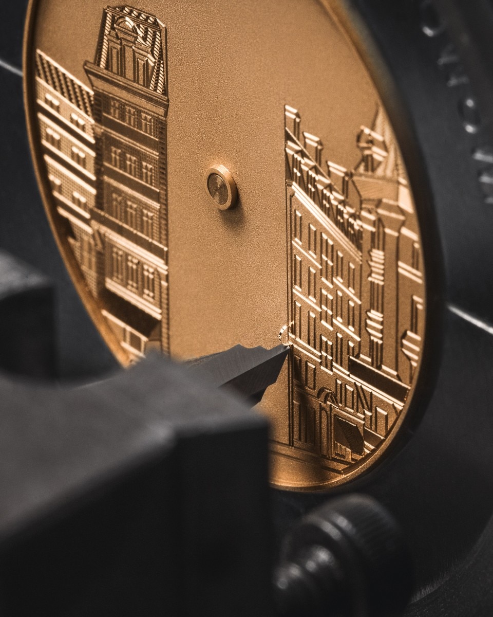 Engraving process of a gold watch dial depiciting historic buildings.