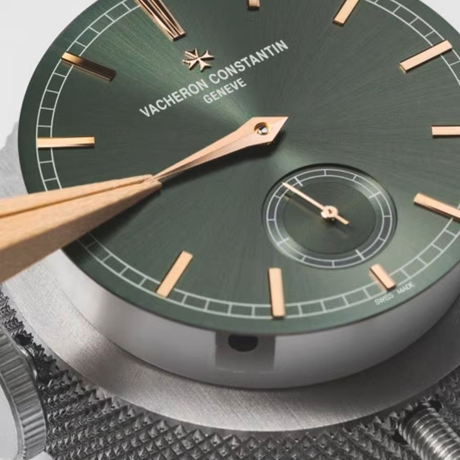 Close-up of a watchmaker's  tool adjusting golden hands on a green watch dial.