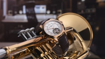 A luxury watch with a brown leather strap placed on a golden trumpet.