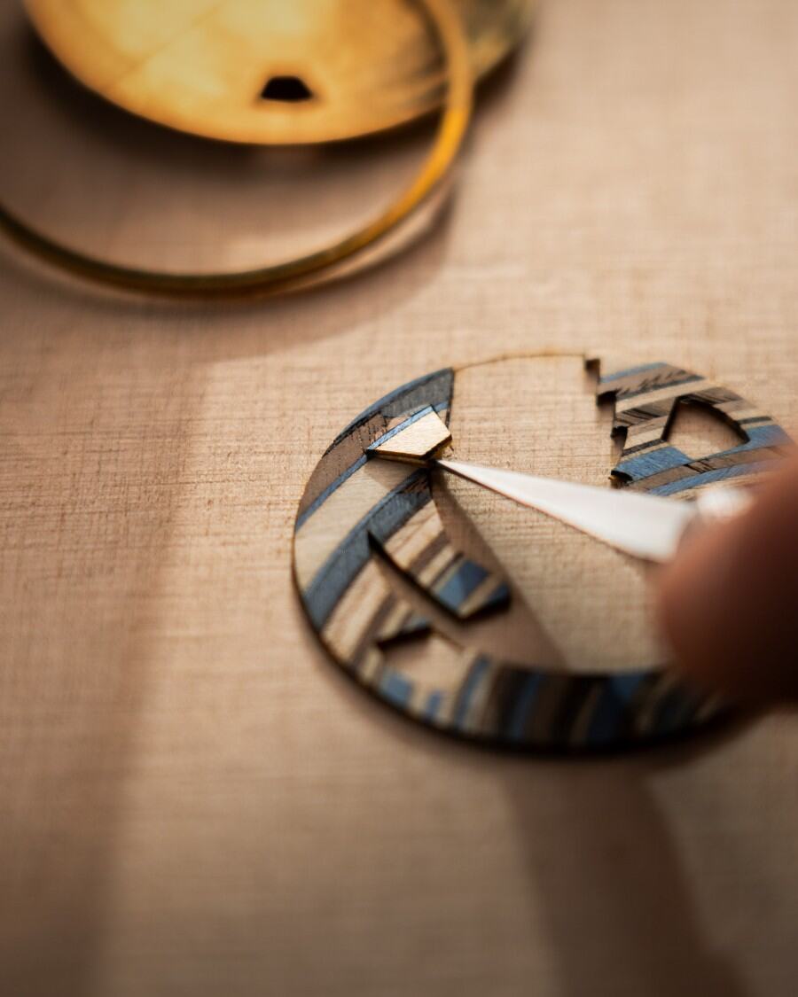Artist using tweezers to place fine handcrafted wooden pieces on the concept watch.