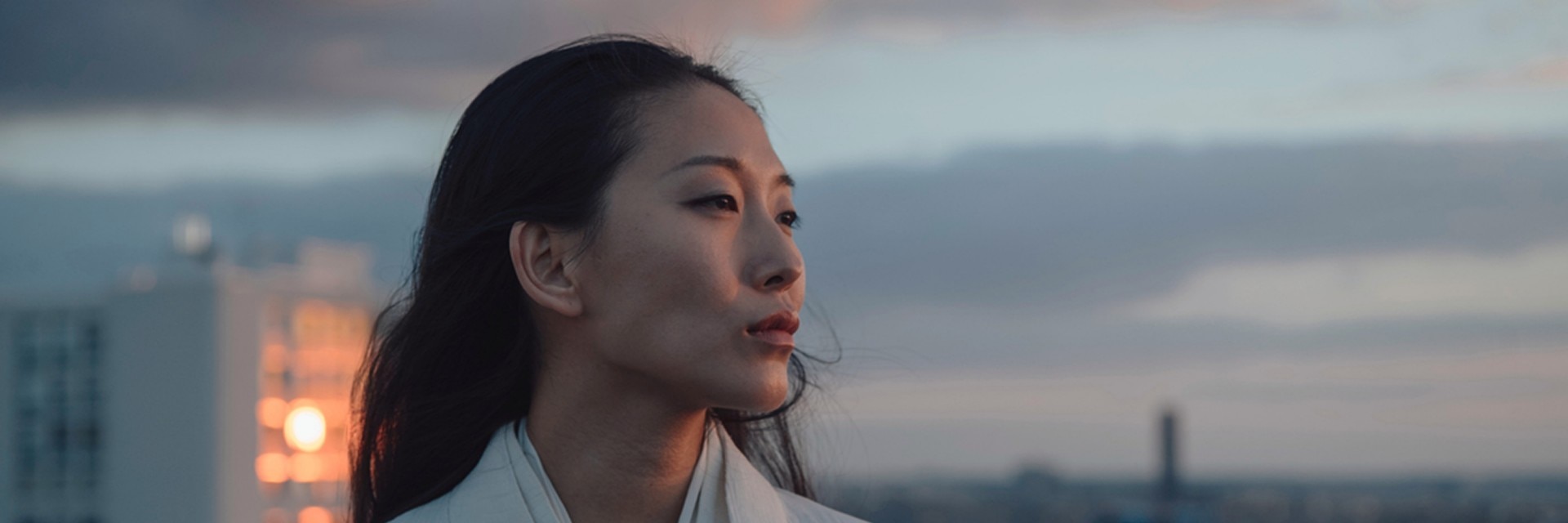 Portrait of a woman at dusk with a cityscape  in the background.