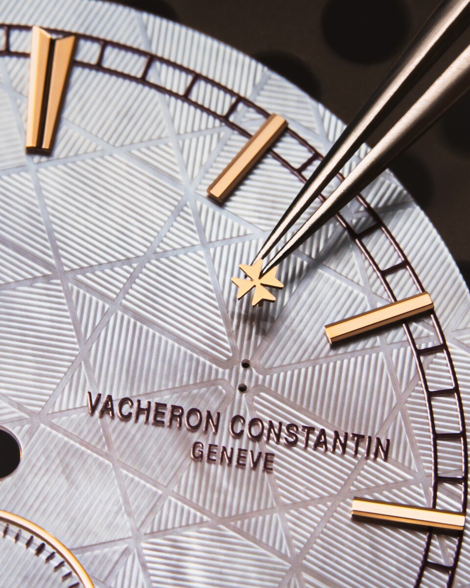 Close-up of gold watch hands being placed on a petterned dial.