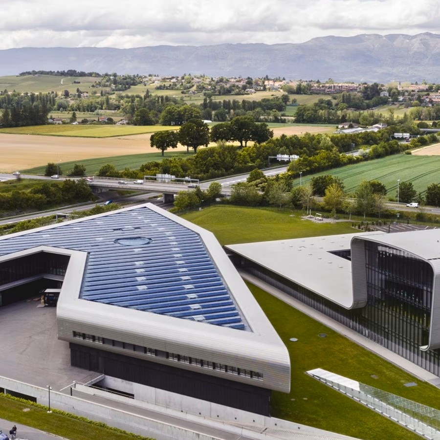 Aerial view of the Vacheron Constantin building with a distinctive modern roof, surrounded by green fields and trees.