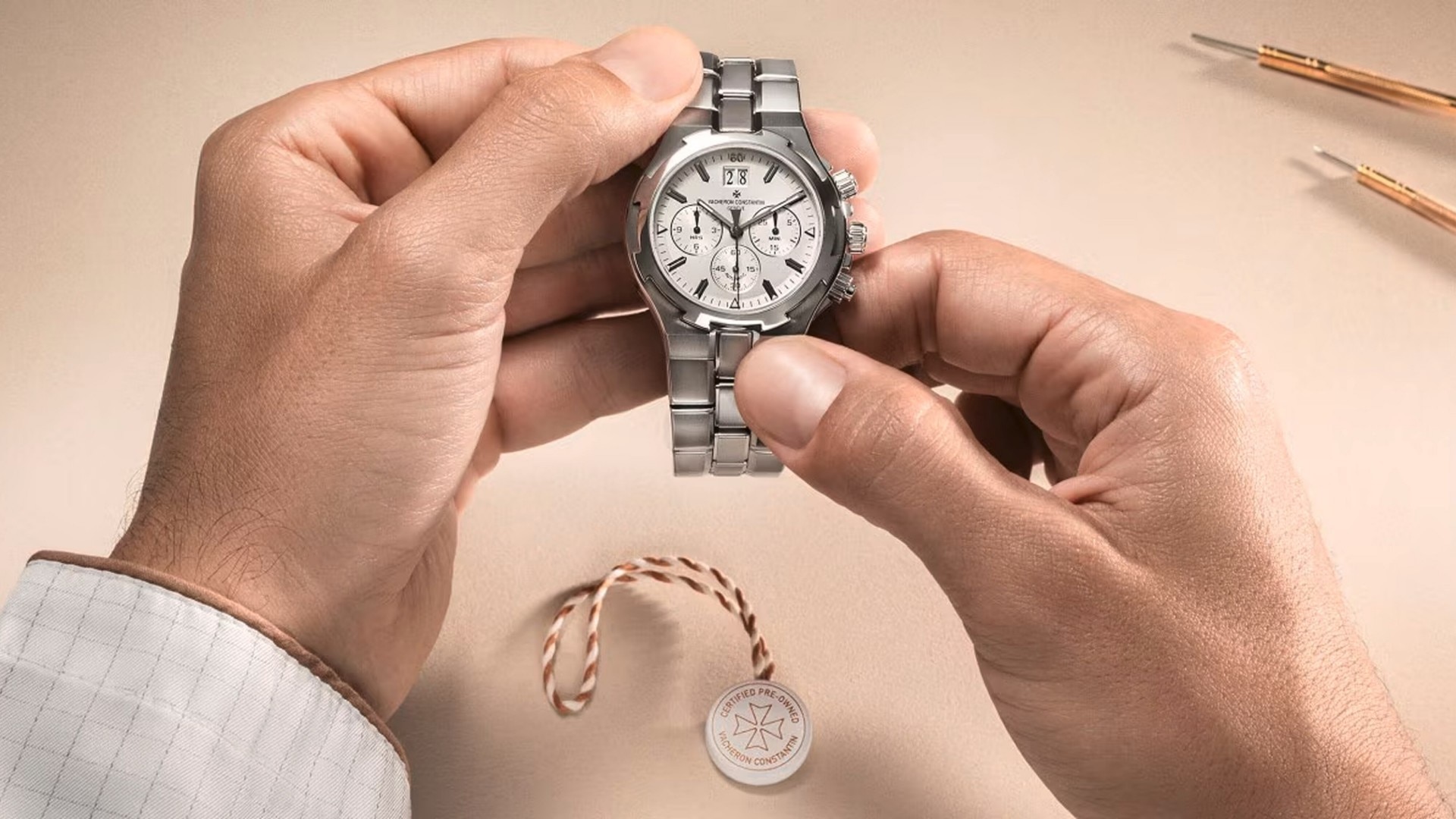 Hands hold a silver metal watch with a white dial on a light background.