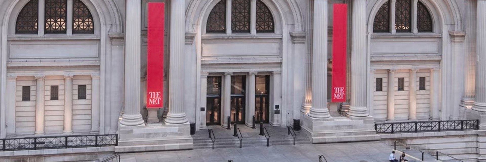 Front entrance of  The Met with red banners and classical architecture.