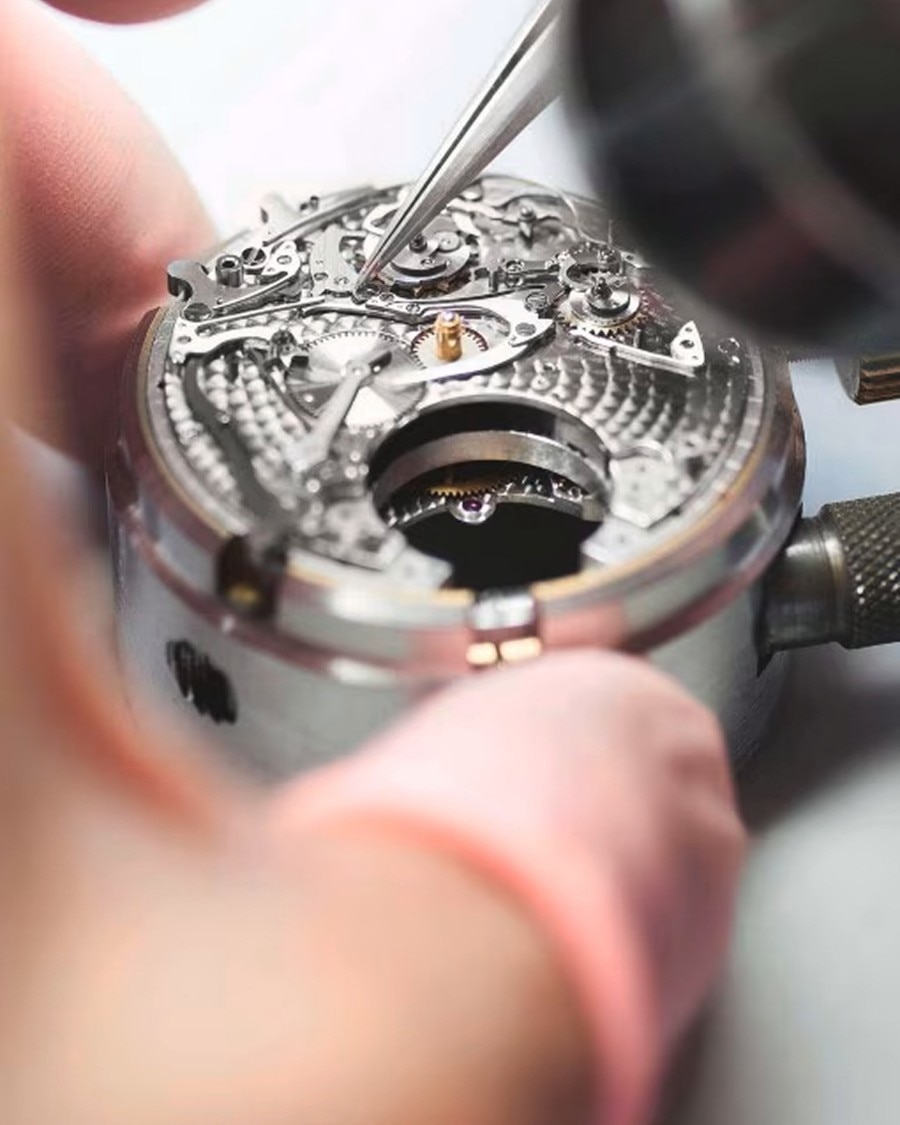 Close-up of a watchmaker assembling a mechanical watch movement using precision tweezers.