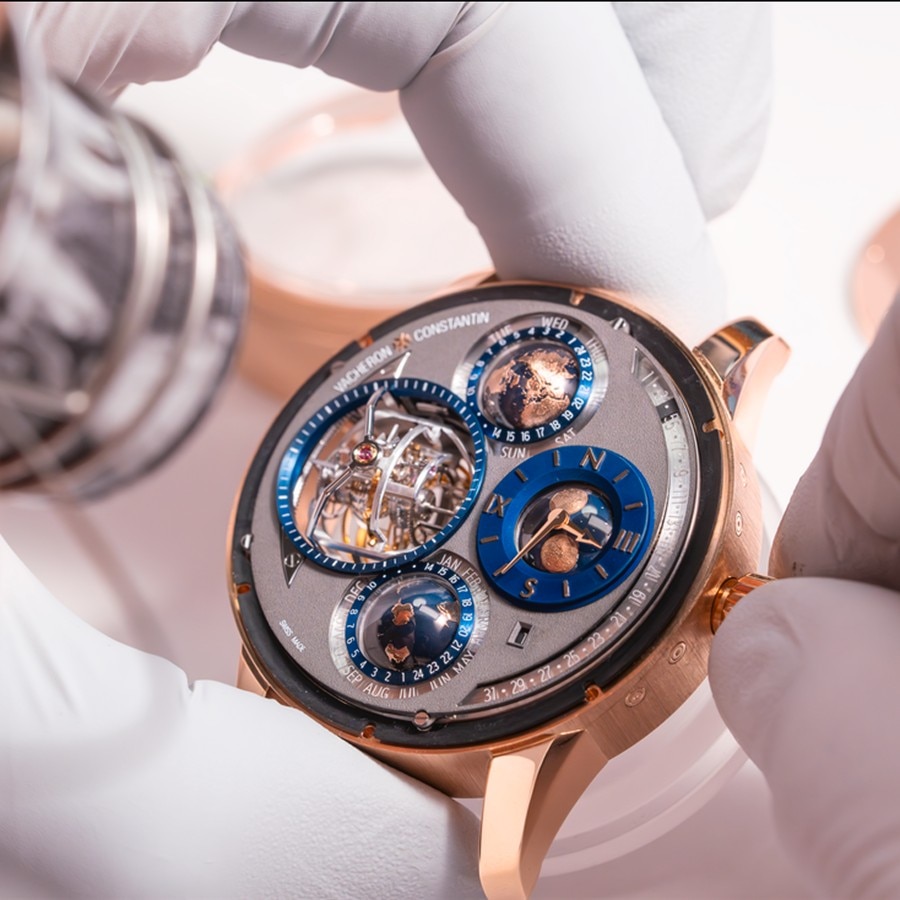 Watchmaker holding an intricate Vacheron Constantin watch with multiple subdials and visible mechanical movement.