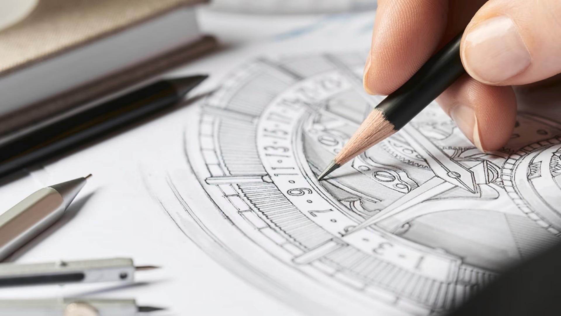 Hand drawing a detailed geometric pattern on paper using a pencil, with drawing tools beside.