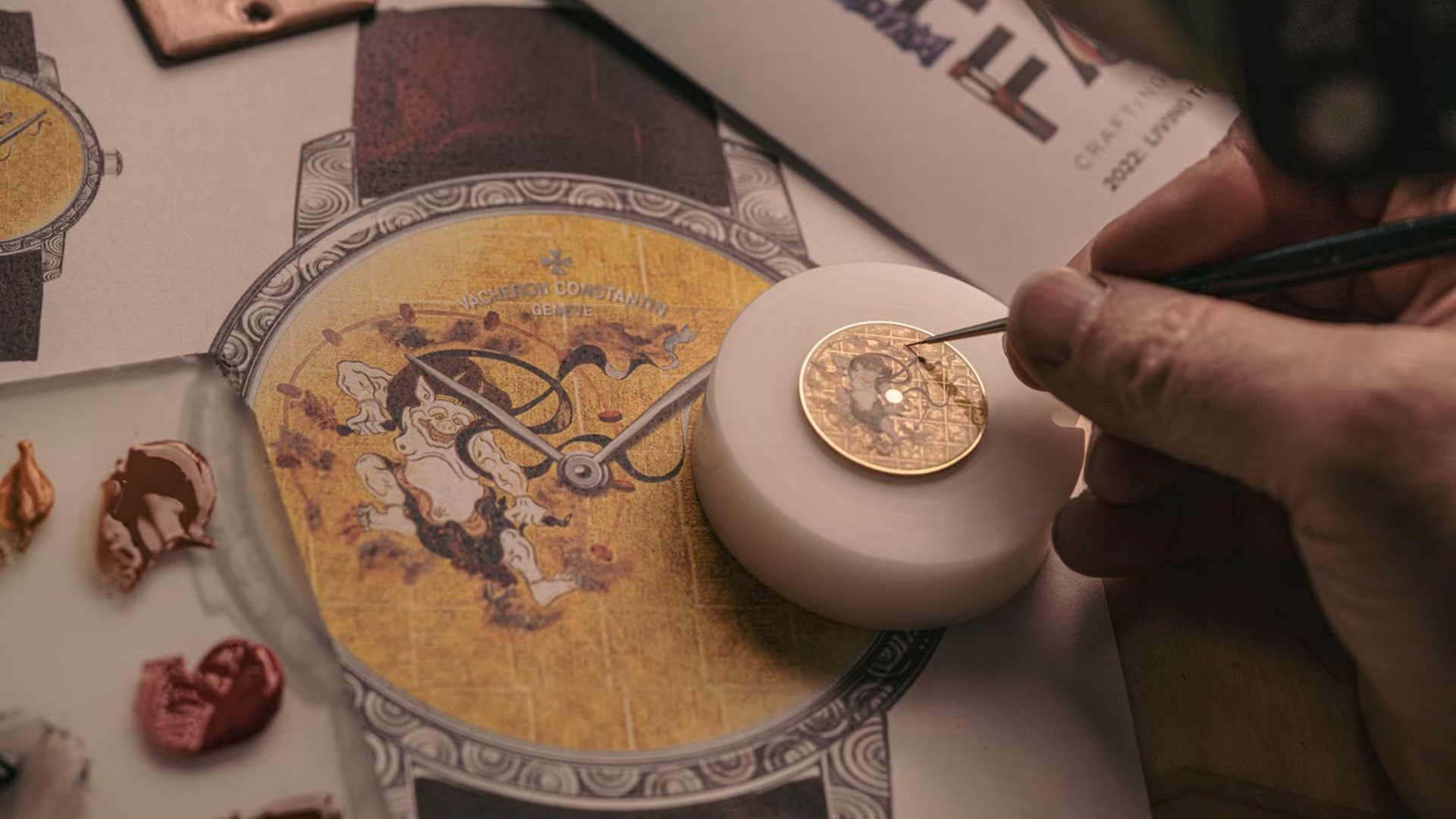 Watchmaker applying paint to a yellow watch dial with an illustration of a figure, surrounded by other tools and designs.