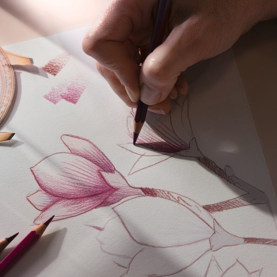 A hand drawing floral designs with a pink colored pencil on white paper.