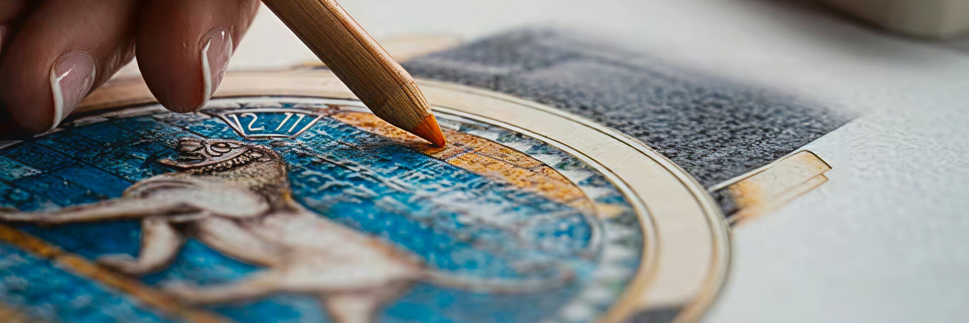 Artisan painting blue and gold details on a watch dial featuring a sculpted figure using a fine brush.