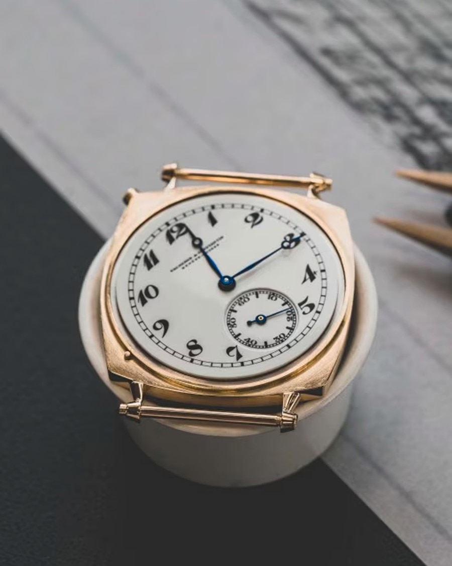 经久耐用 Top view of a vintage-style Vacheron Constantin watch with a white dial, black numerals, and small seconds subdial, placed on a dark surface.