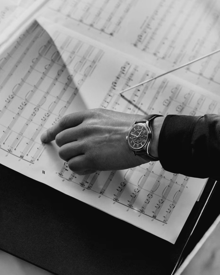 Black and white image of a person wearing a luxury watch while turning pages of a musical score.