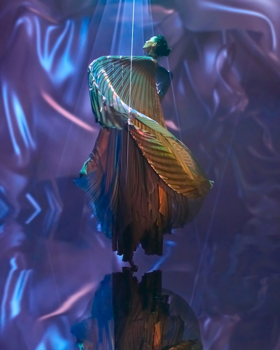 Vibrant abstract illustration of a woman in flowing multicolored garments, surrounded by swirling motion.
