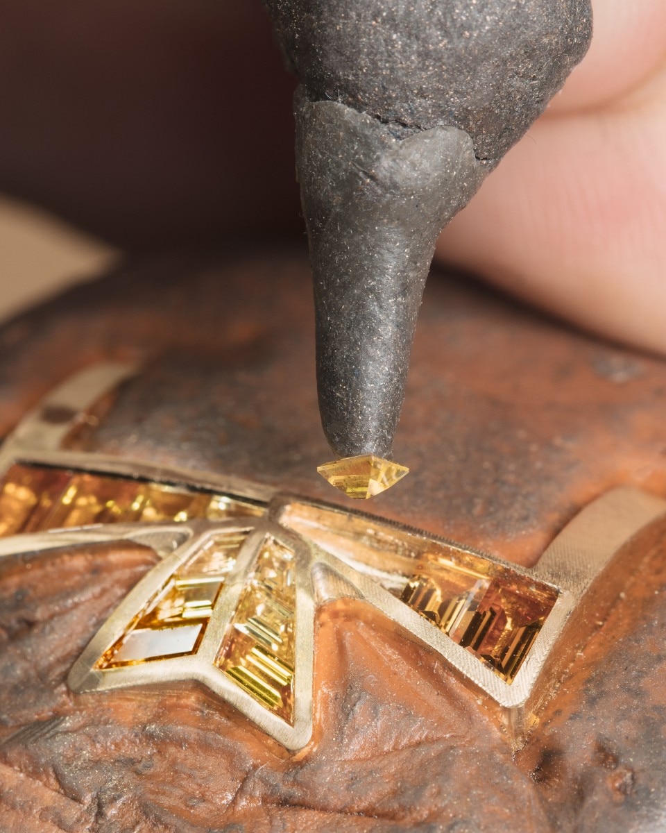 Placing a yellow gemstone into a V-shaped golden setting with precision.