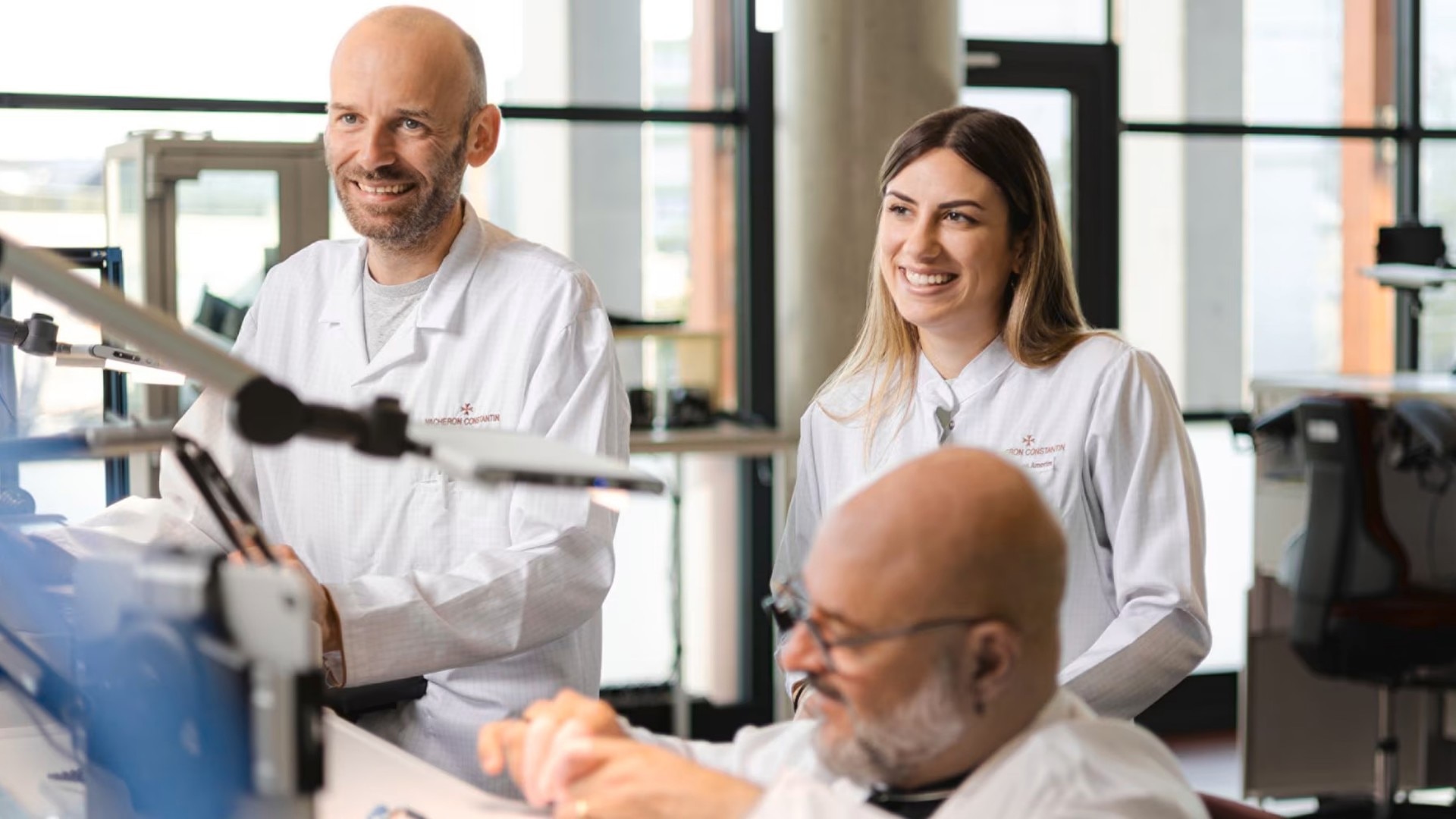 Team of watchmakers smiling and working together in a bright workshop with microscopes and tools.