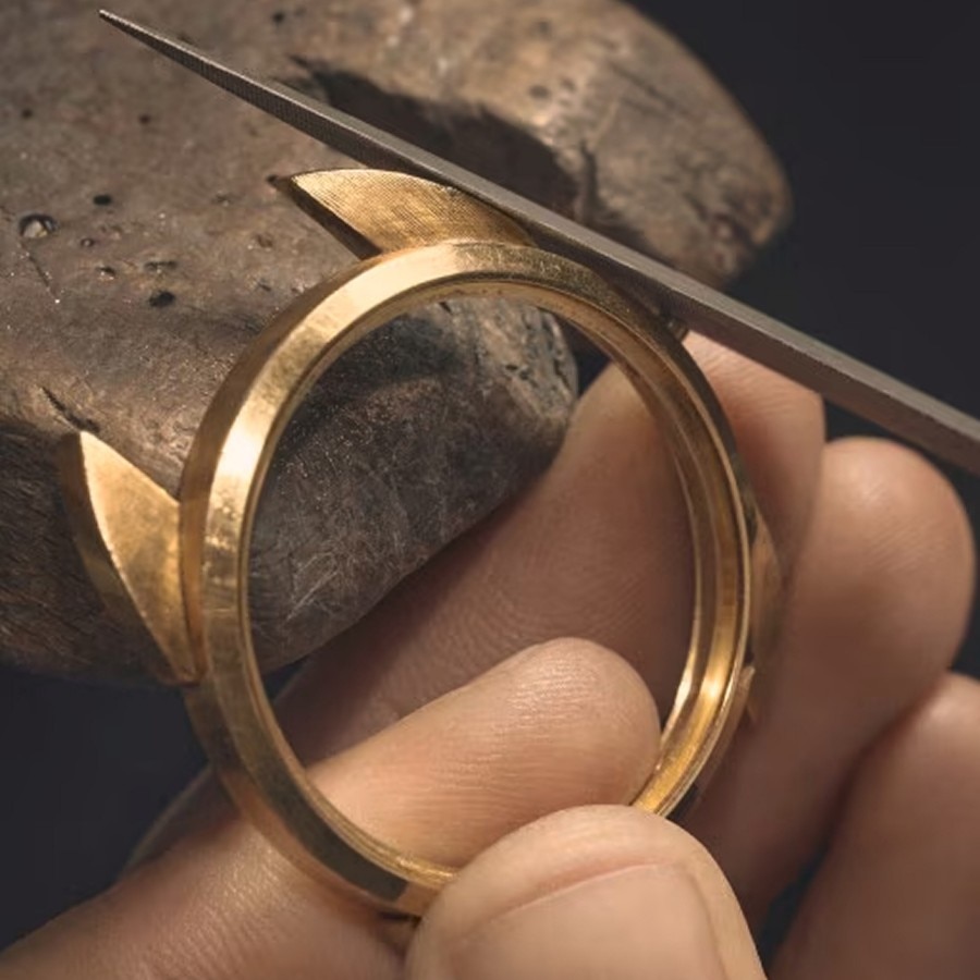 Watchmaker holding a gold watch case while using a precision tool for fine adjustment.