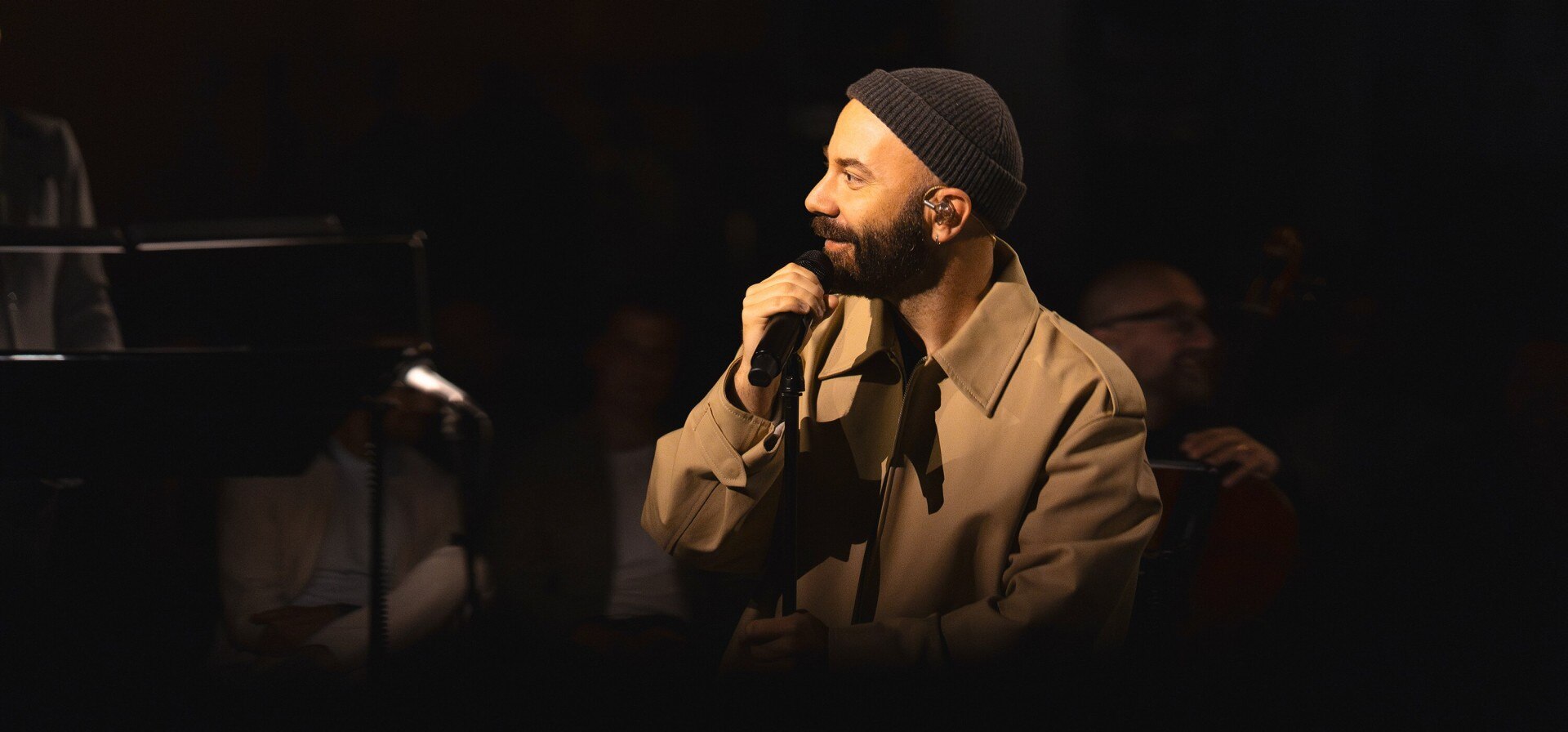 Woodkid 手持麦克风,戴着无檐小帽和外套,在舞台上表演。