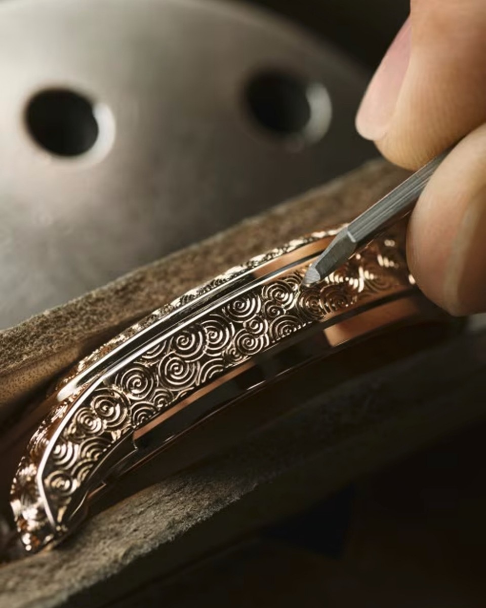 Close-up of a craftsman engraving intricate patterns on a watch case using fine tools.