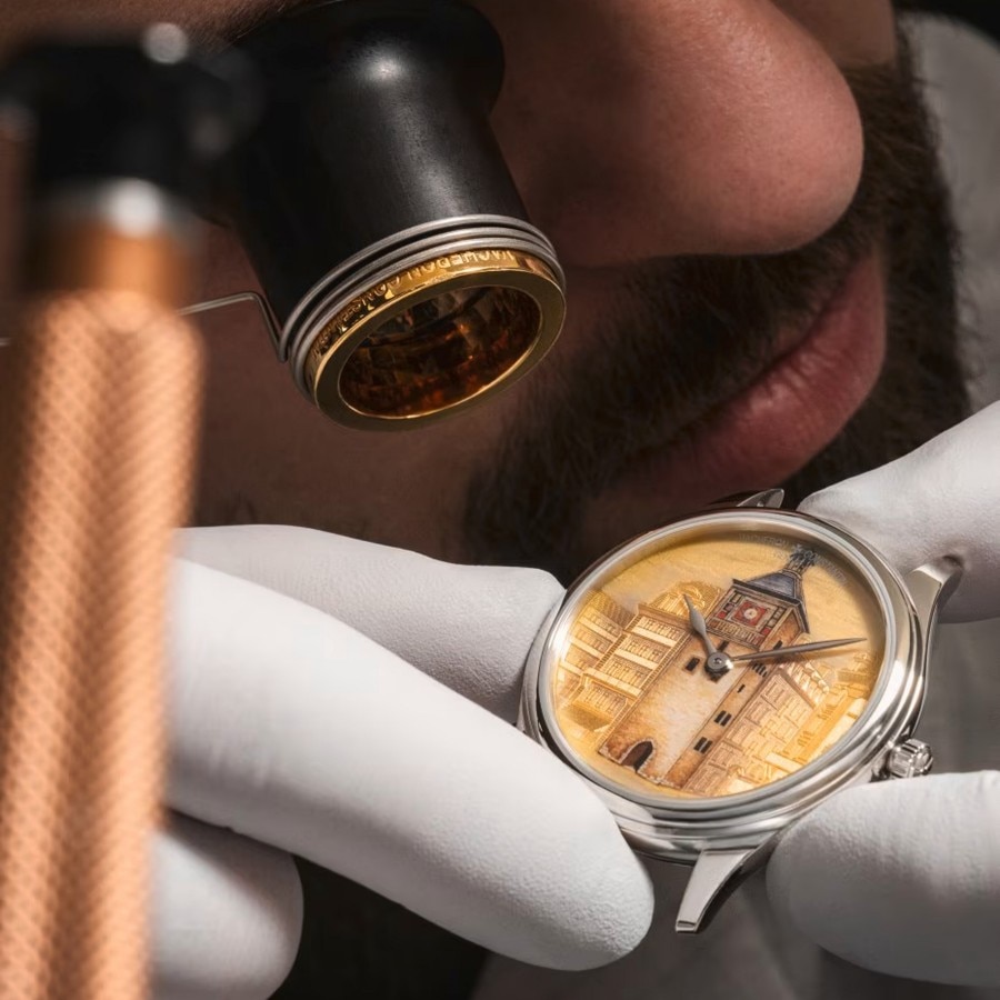 Watchmaker inspecting an enamel-dial luxury watch with a loupe.