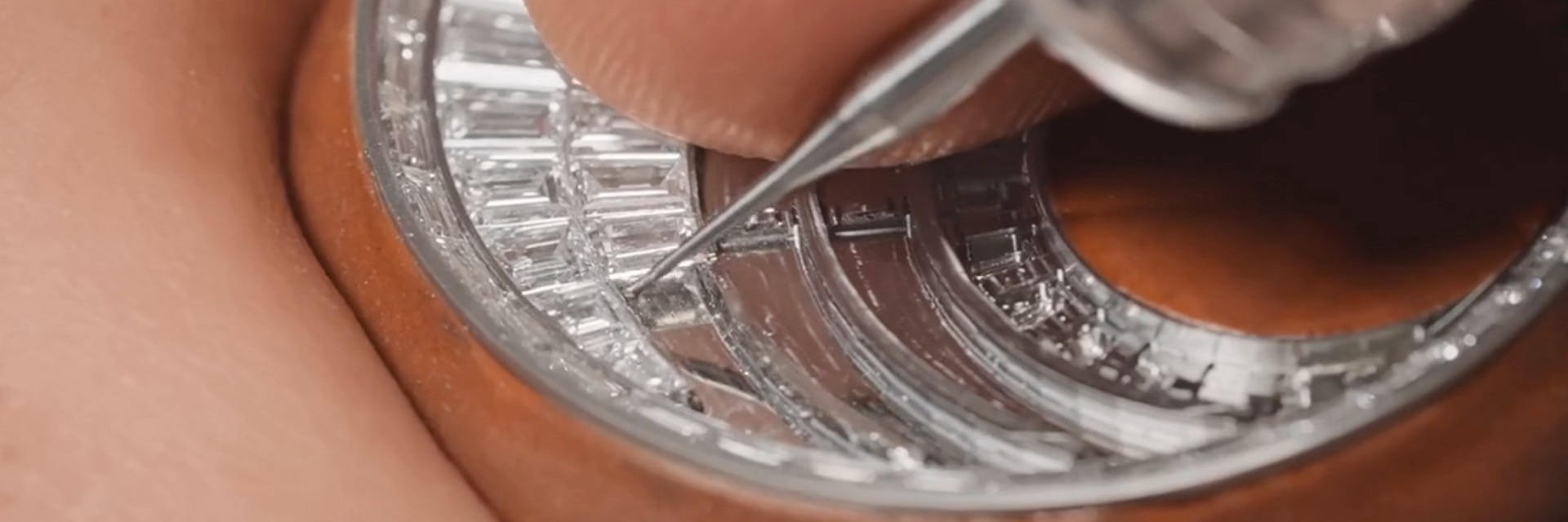 Jeweller setting baguette-cut diamonds into a circular watch case.