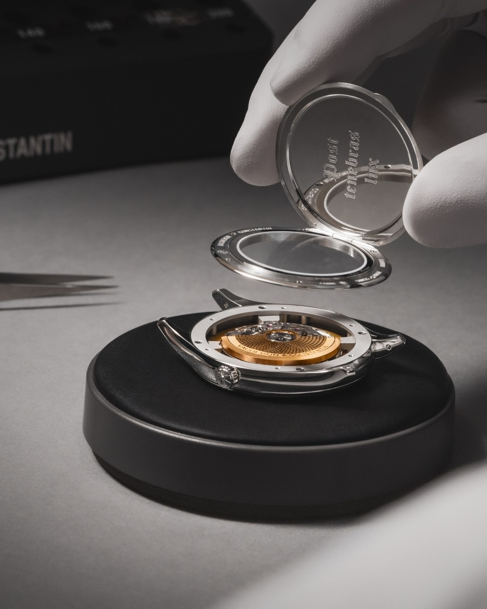 Watchmaker assembling a timepiece, placing a transparent watch crystal over the dial.