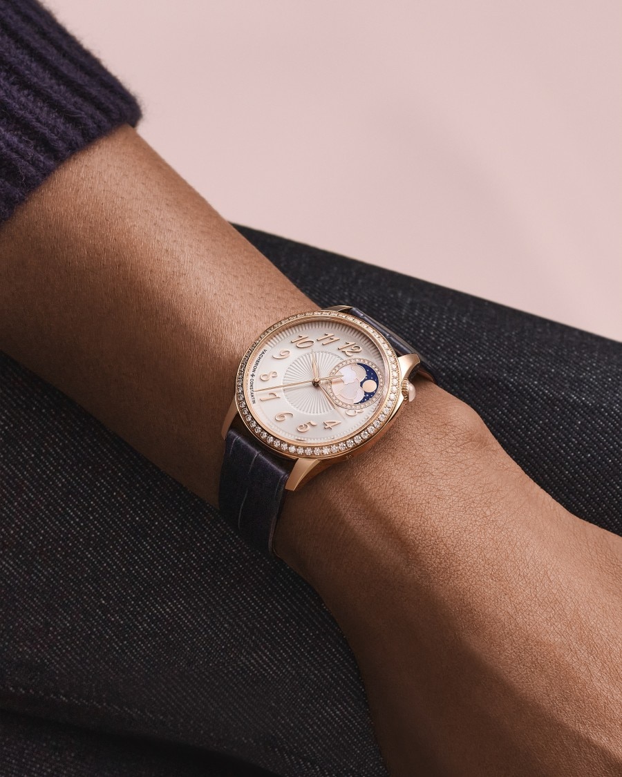  Égérie watch with white dial and gold case on wrist in dark sleeve.