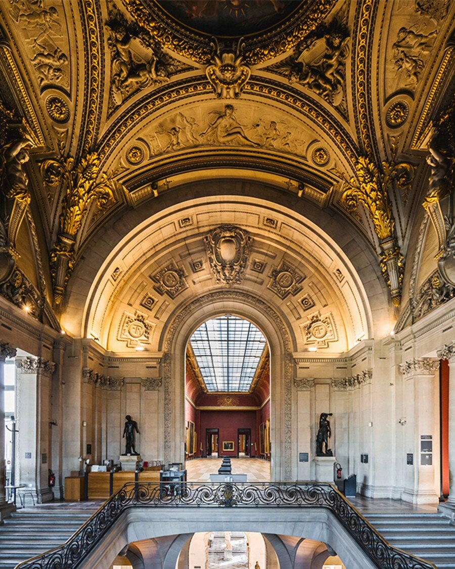 Ornate museum hall with vaulted golden ceiling and arched window.