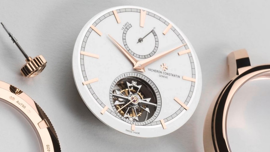 Close-up view of a watch case with light gray and gold elements and with a partially visible watch mechanism