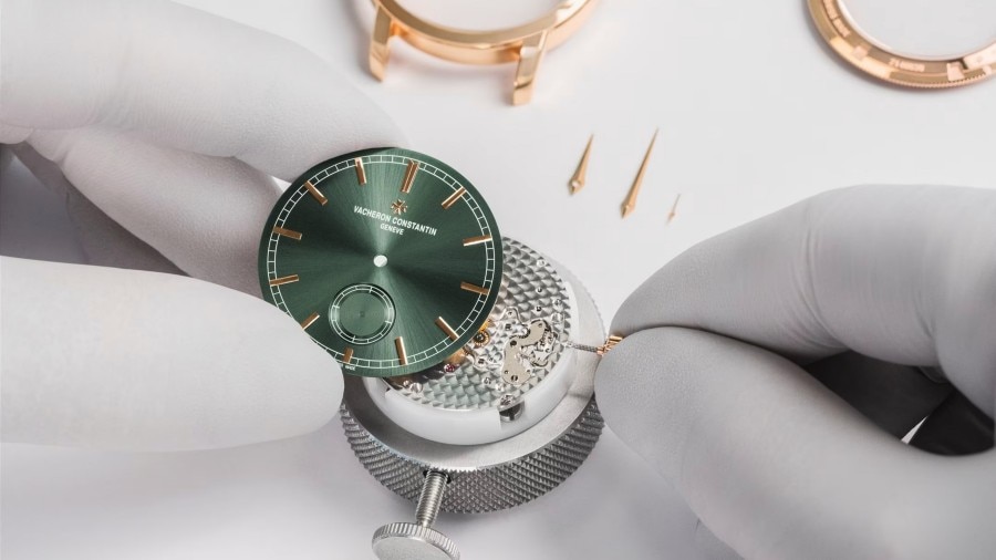 Two human hands are setting up a watch with a leather strap and a white dial with gold hands and frame
