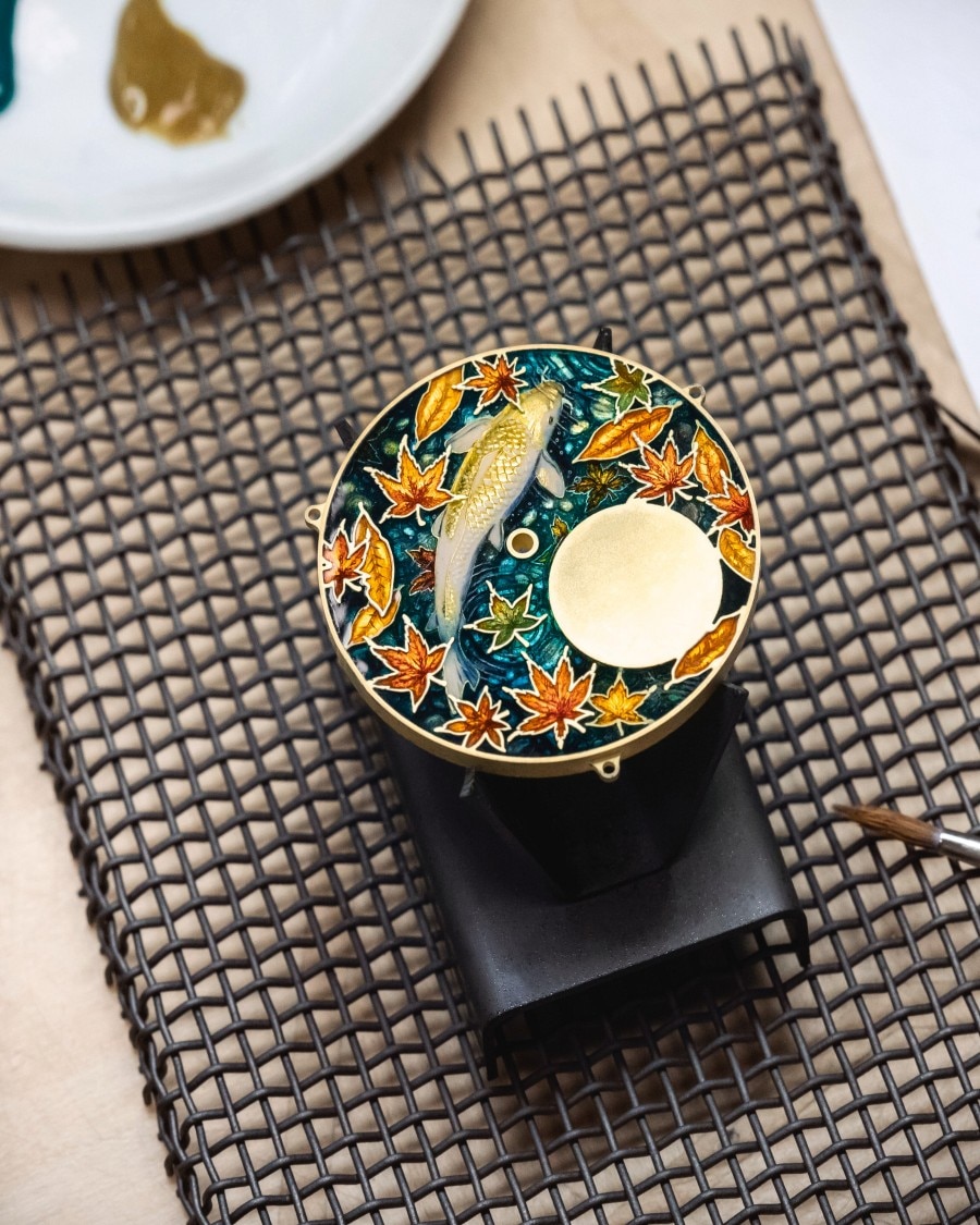 Hand-painted watch dial featuring a koi fish and autumn leaves, showcasing traditional enamel artistry.