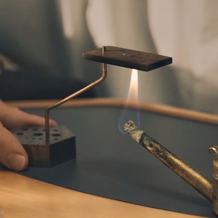 Watchmaker using a small torch to heat a component on a soldering stand during the fabrication process.