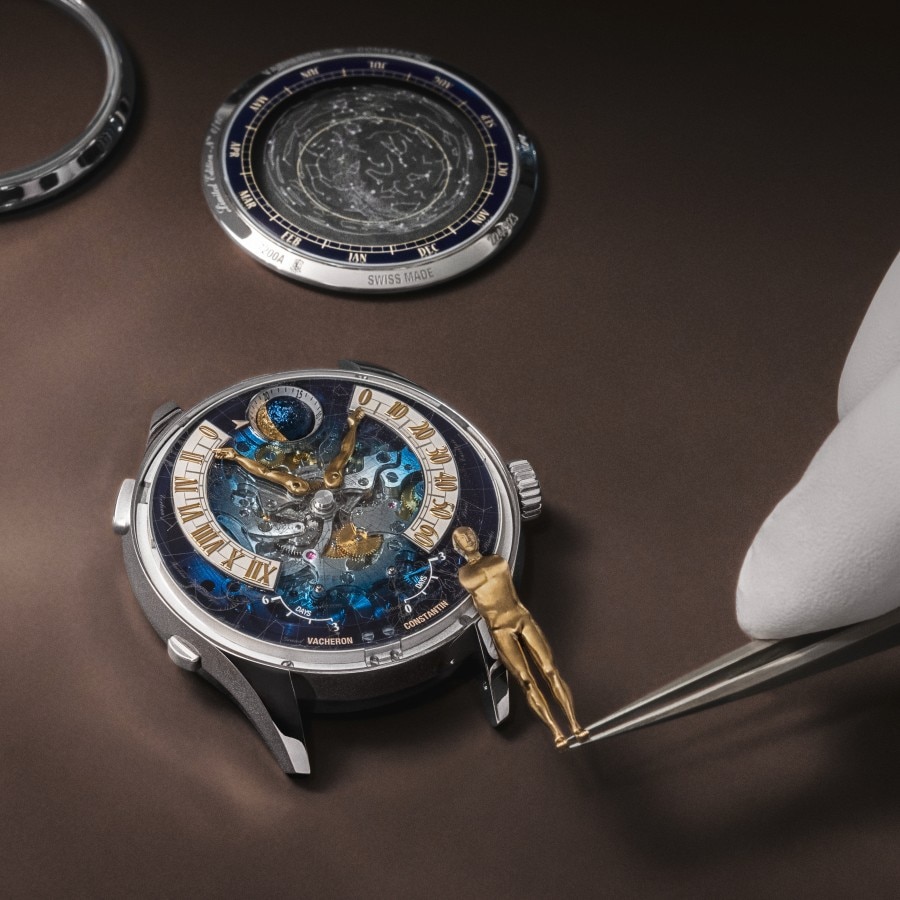 Watchmaker assembling a human body-shaped element onto a dial movement with tweezers.