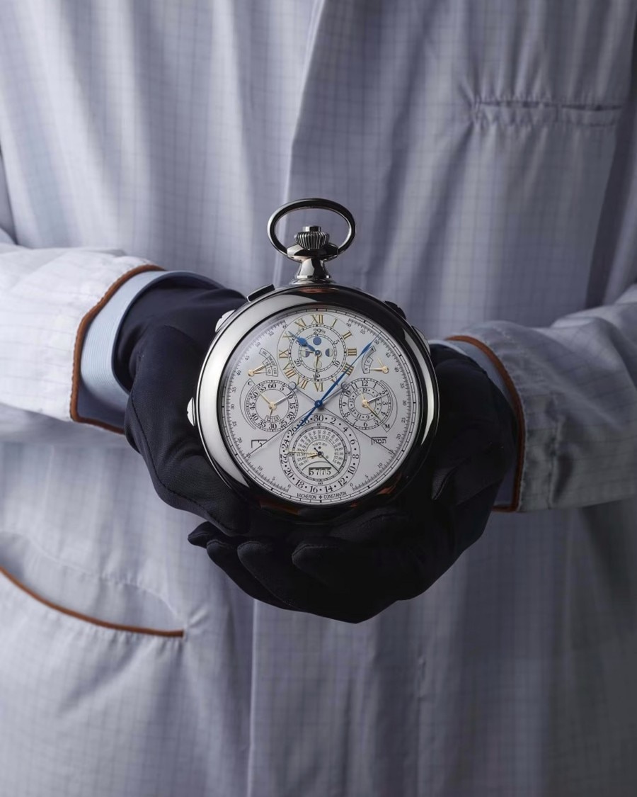 Gloved hands holding a vintage  pocket watch against a white lab coat.