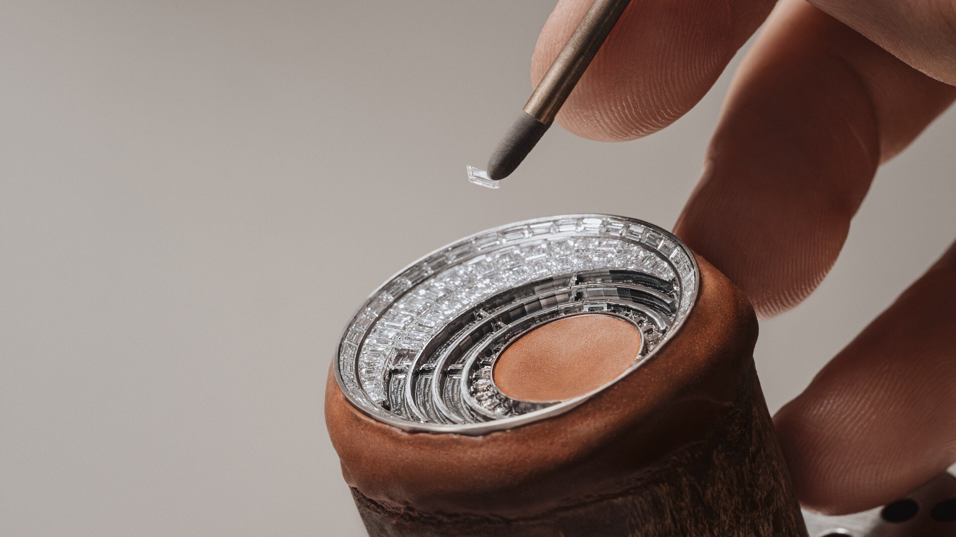 Jeweler's hand placing diamonds into a concentric setting on a watch component using a fine-tipped tool.