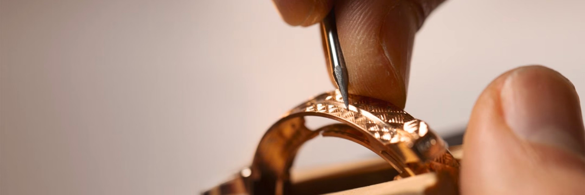 Detailed view of a hand engraving a decorative pattern onto a golden watch case using a specialized tool.