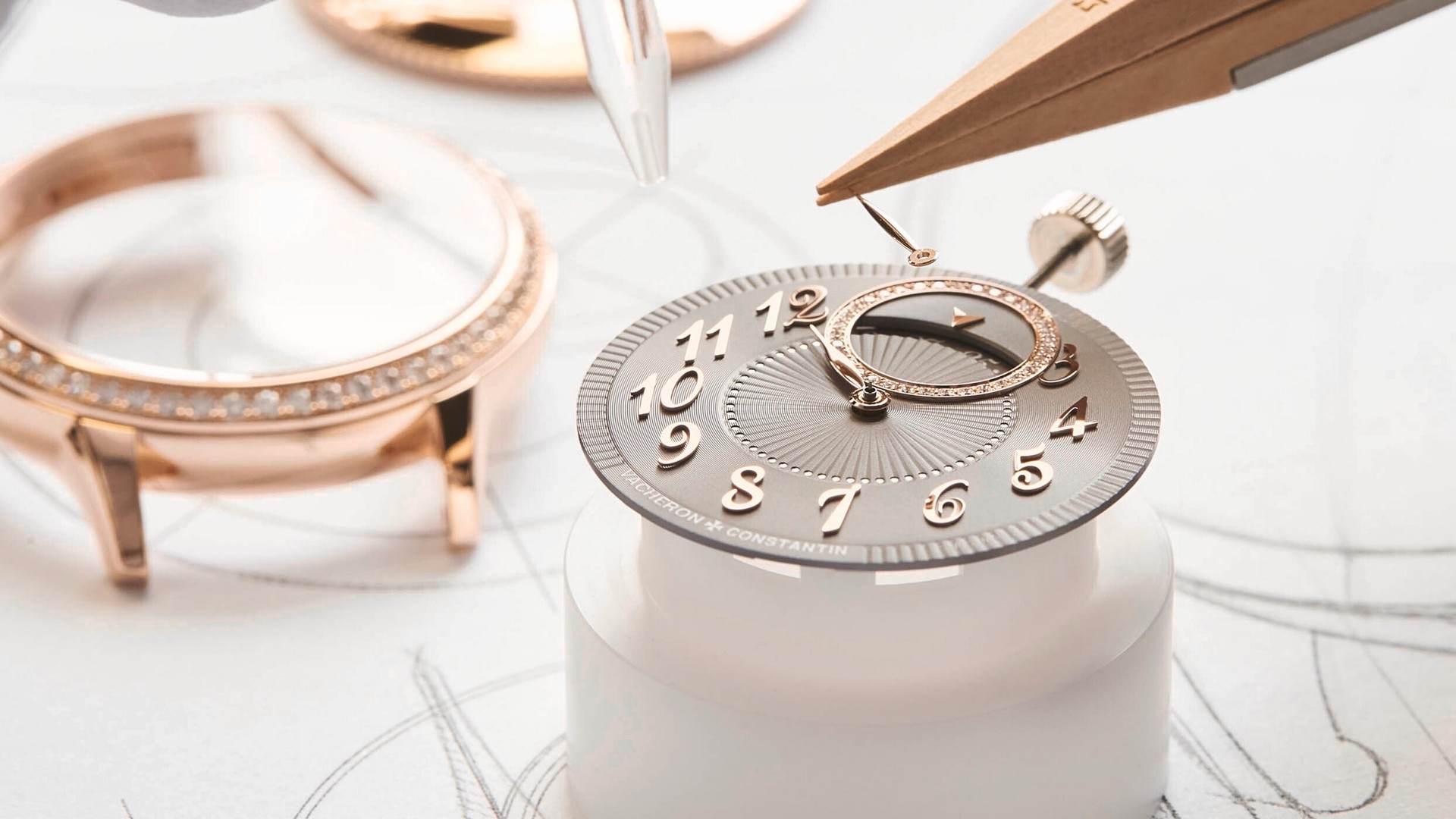 A gold hand is being precisely placed on a grayish base of the clock with gold details and numbers