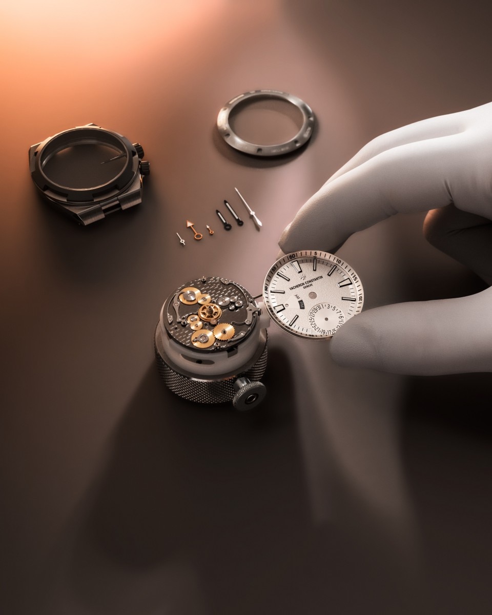 View of small watch parts on a table including crown, case back, and other metal components.