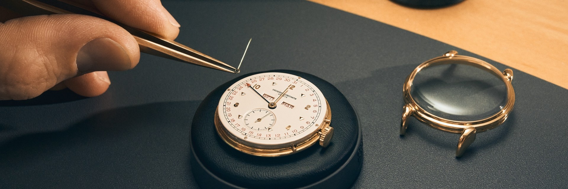 A watchmaker's hand precisely positions a clock hand on a white and gold watch.