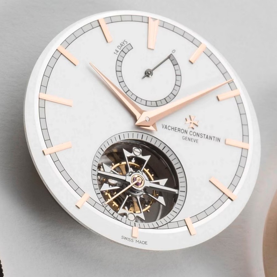 Watch case with light gray and gold elements and with a partially visible watch mechanism